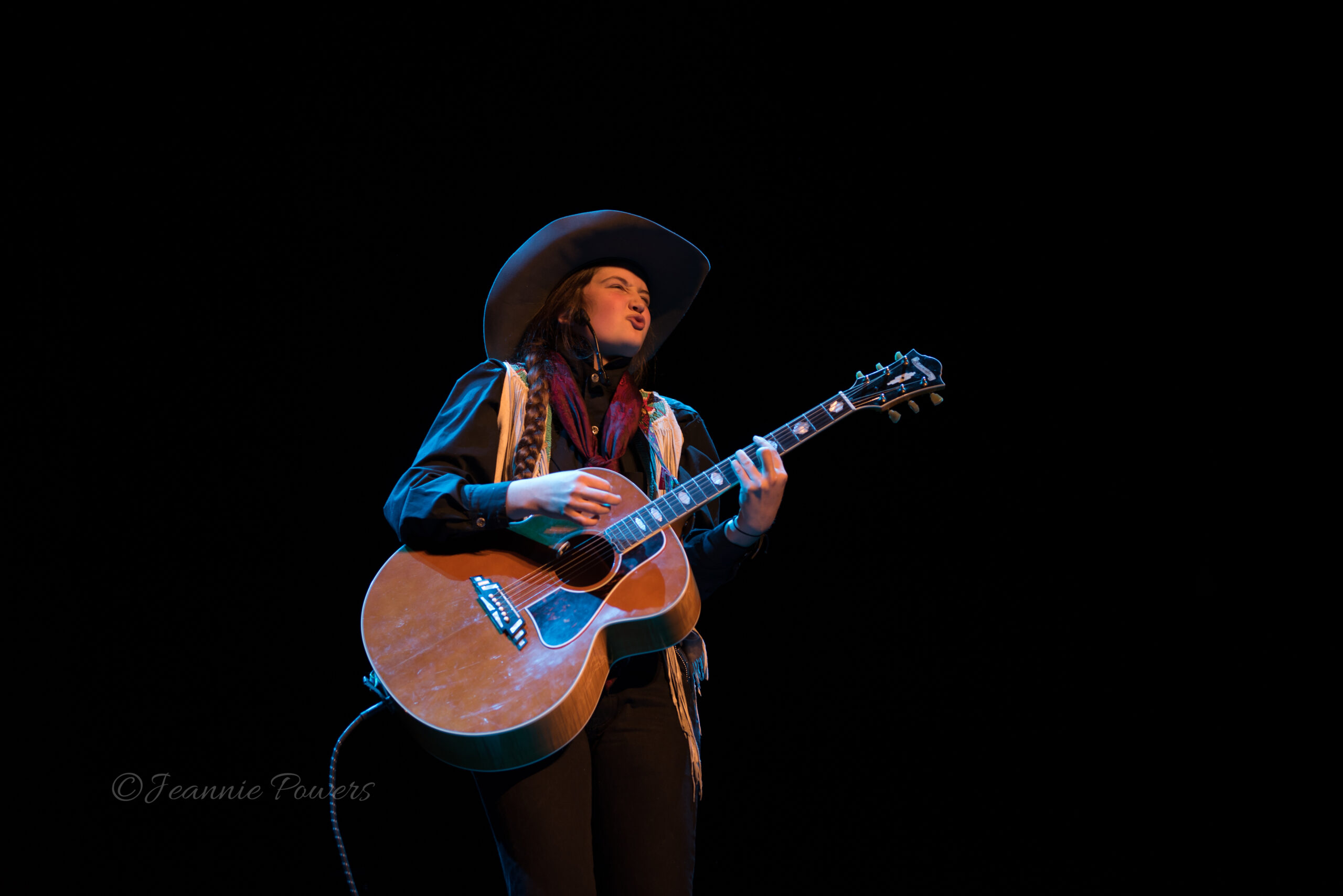 Jeneve Rose Mitchell performing on stage with acoustic guitar